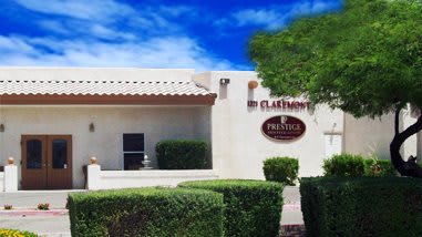 A southwestern-style building surrounded by neatly trimmed bushes and a small tree.