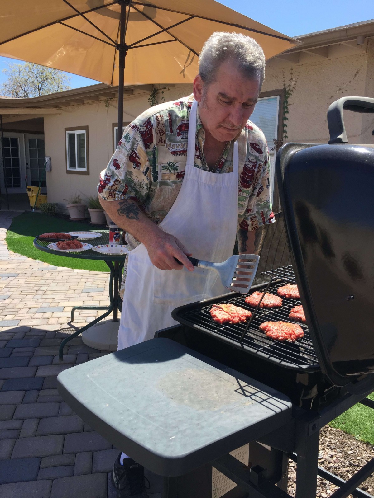 A man grilling burgers on a barbecue in the backyard on a sunny day.
