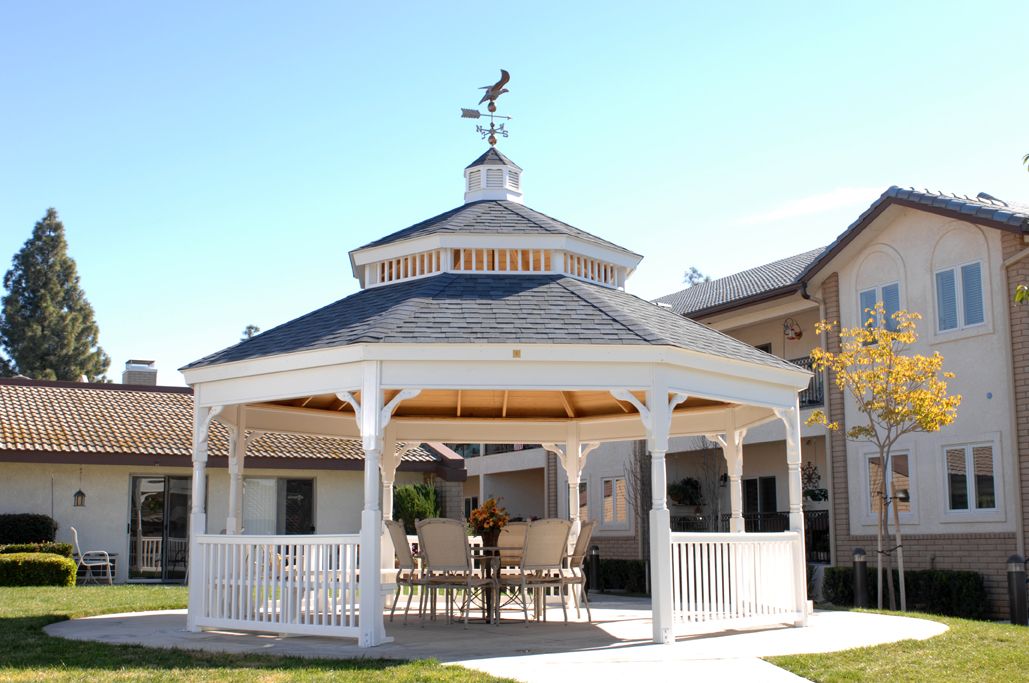 A white wooden gazebo with a weather vane on top, set in an outdoor area.