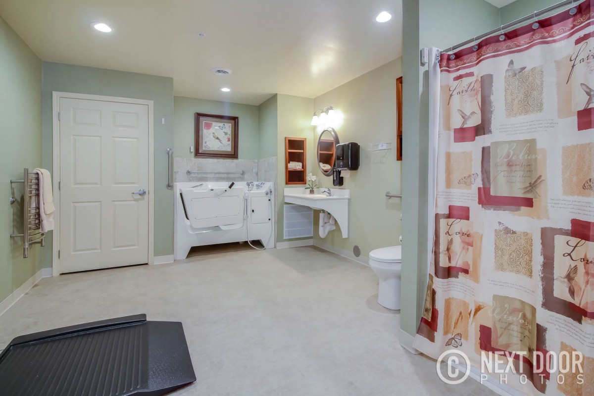 An accessible bathroom featuring a shower with grab bars, toilet, sink, and a wall mirror.