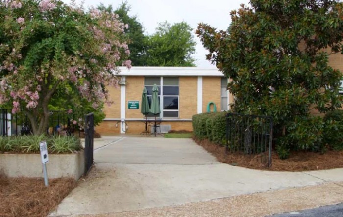 A small brick building with a driveway and surrounding greenery.