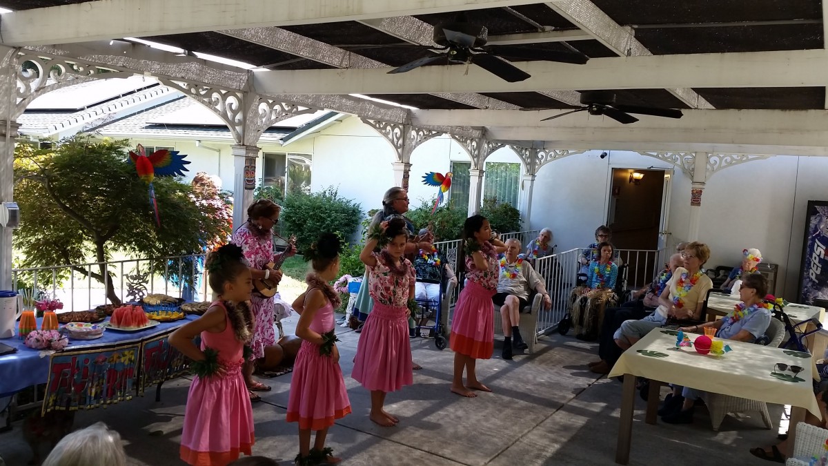 A group of hula dancers performing at an outdoor event, watched by an audience.