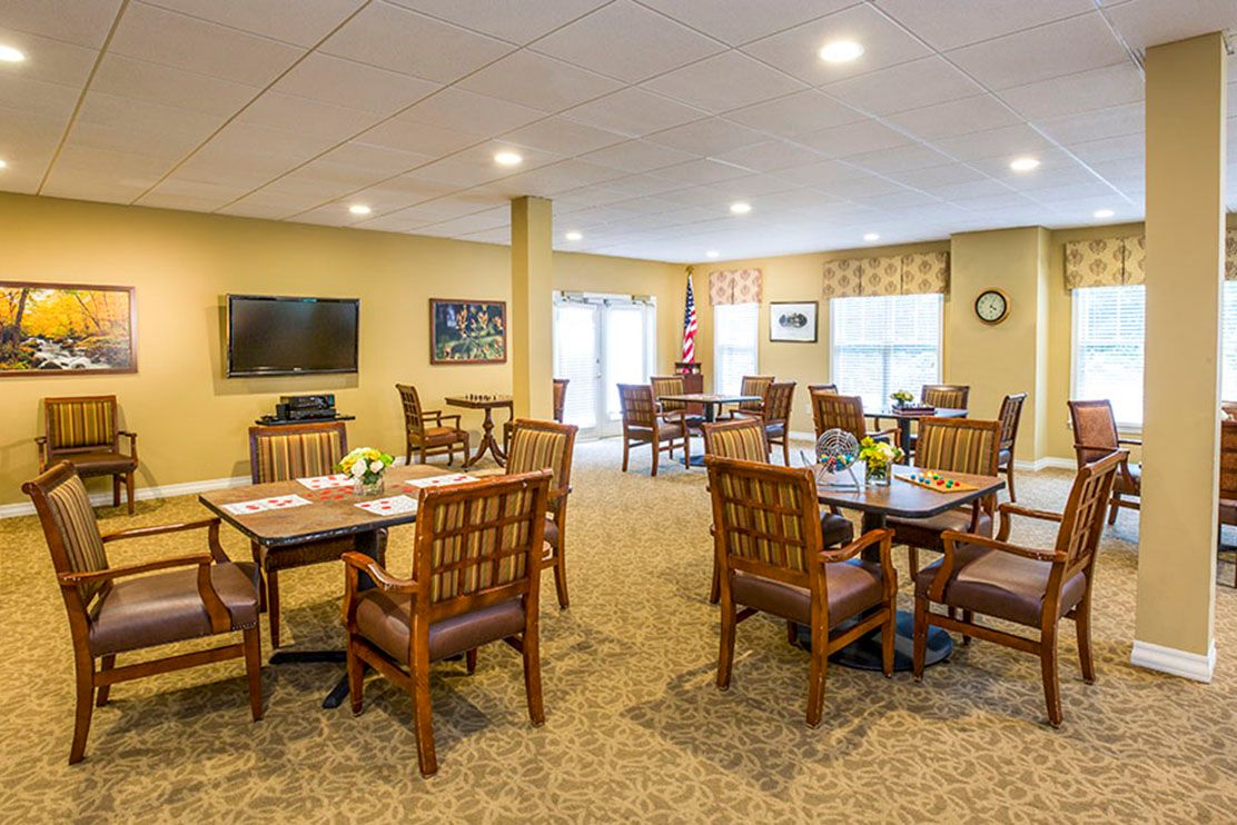 A cozy dining area with wooden tables and chairs, featuring a television and large windows.