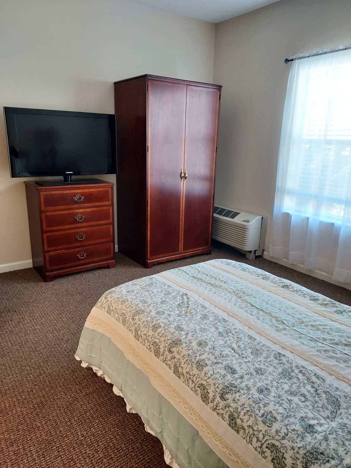 A cozy bedroom with a wardrobe, dresser, and television.