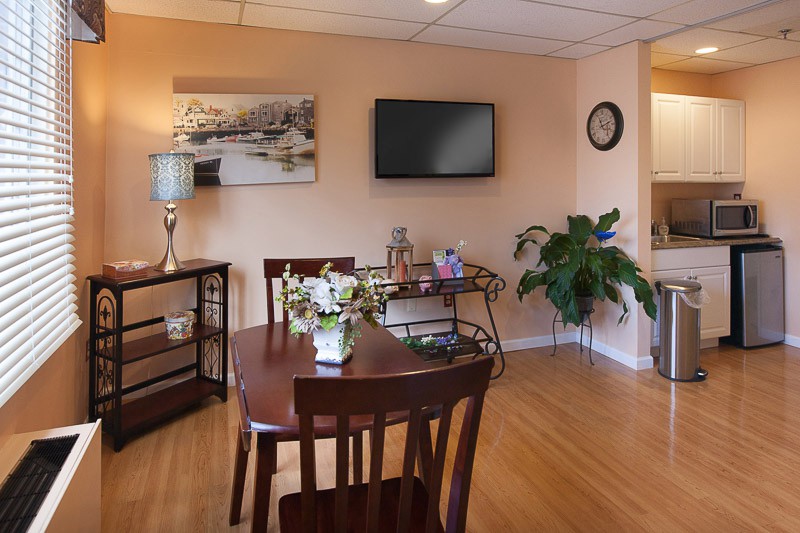 A cozy dining room with a wooden table and chairs, a wall-mounted television, and decorative elements such as a painting, lamp, and plant.