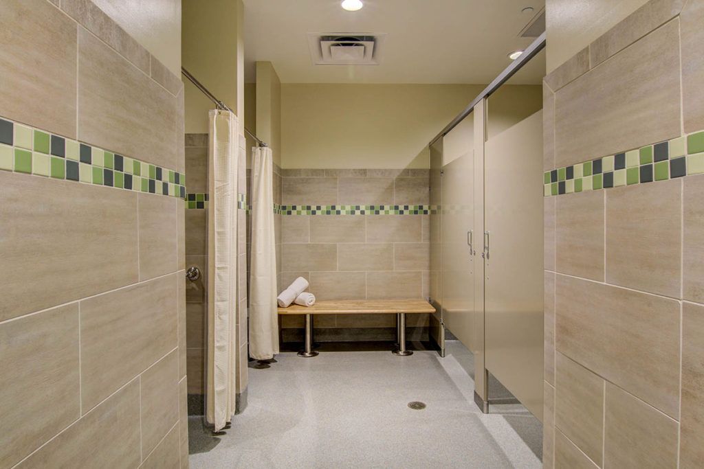 A clean and tidy locker room shower area with tiled walls, a wooden bench, and privacy curtains.