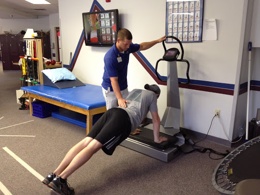 A personal trainer assists a client with push-ups on a vibrating platform.