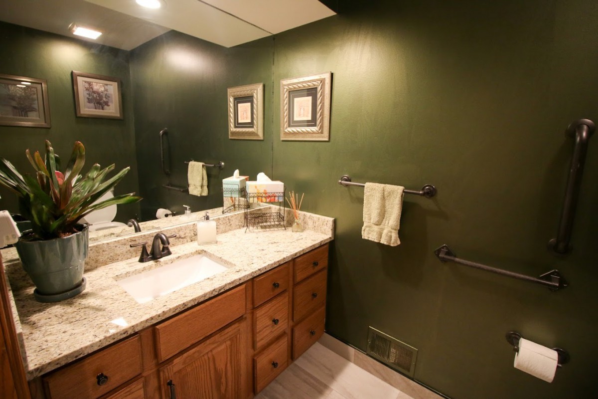 A cozy bathroom with green walls, a wooden cabinet, and decorative items on the countertop.