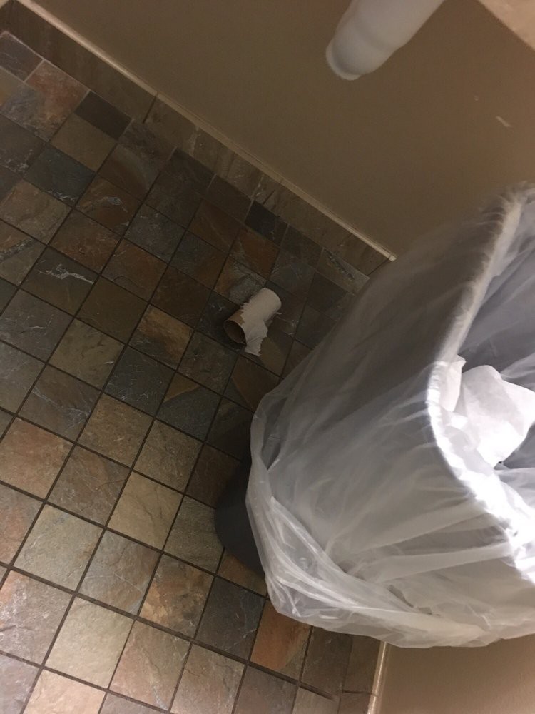 A trash can with a plastic liner stands on a tiled floor indoors.