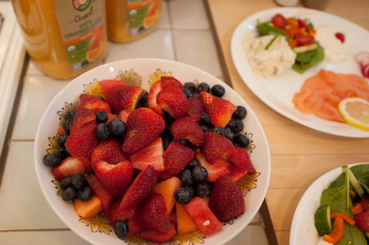 A colorful bowl of fruit salad featuring strawberries, blueberries, and melon on a breakfast table.