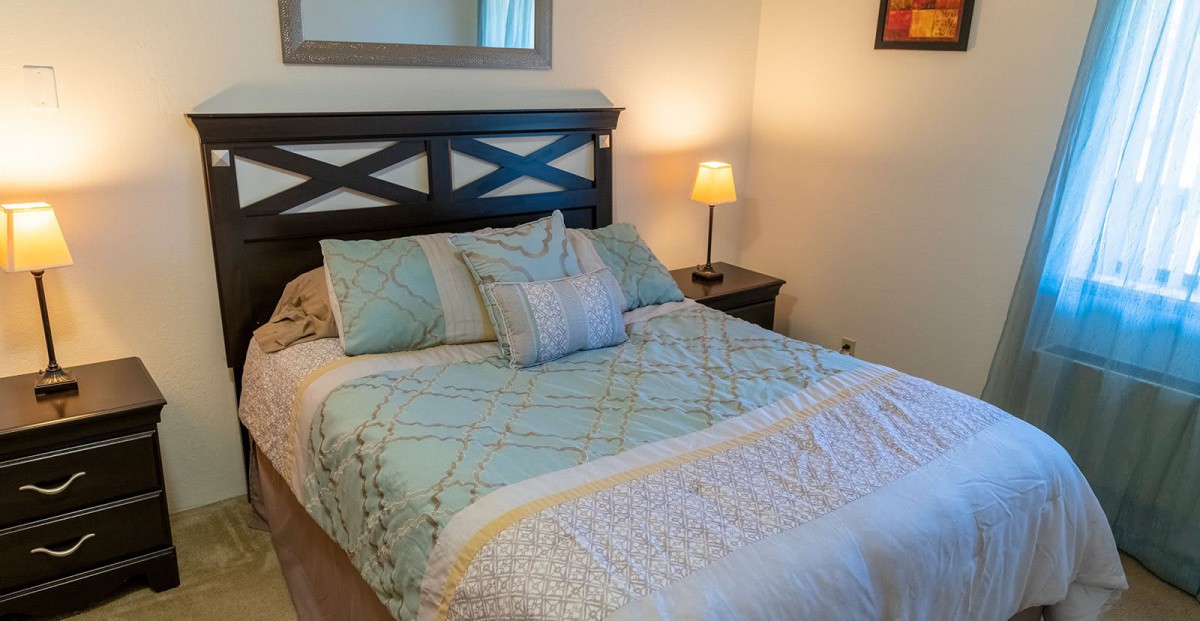 A cozy bedroom with a neatly made bed, decorative pillows, and a lamp on the nightstand.