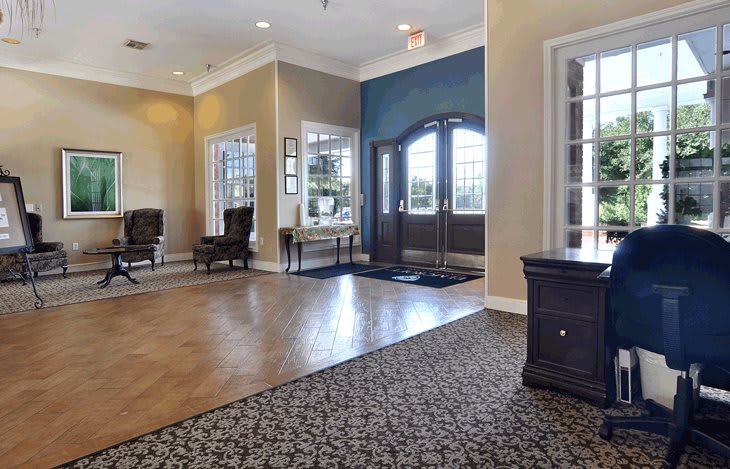 A spacious lobby with a combination of carpet and wood flooring, featuring elegant furniture and large windows.
