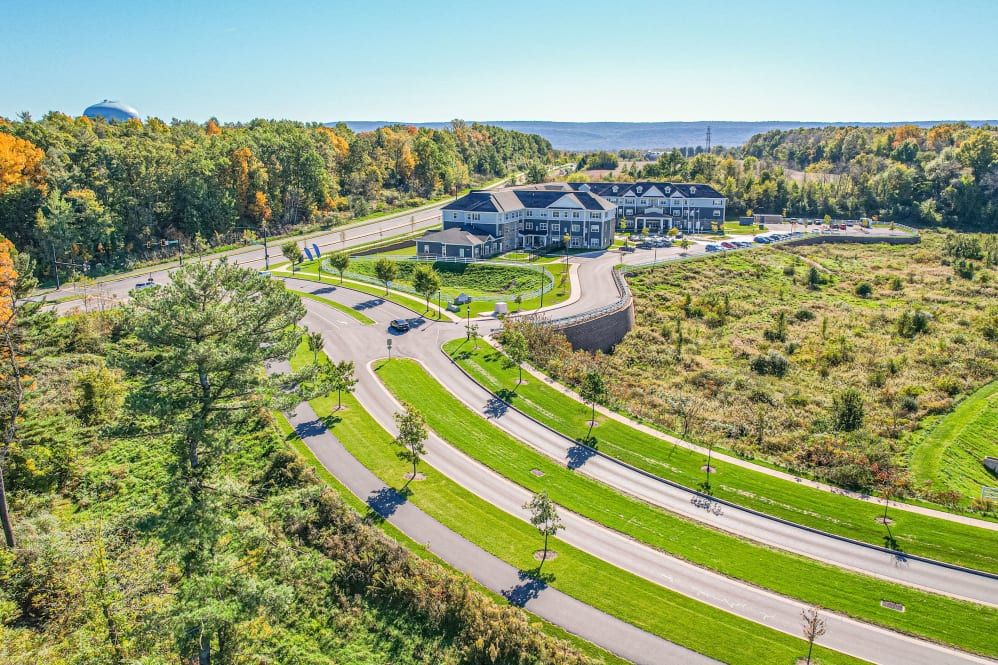 Aerial view of a large building surrounded by landscaped roads and lush greenery on a sunny day.