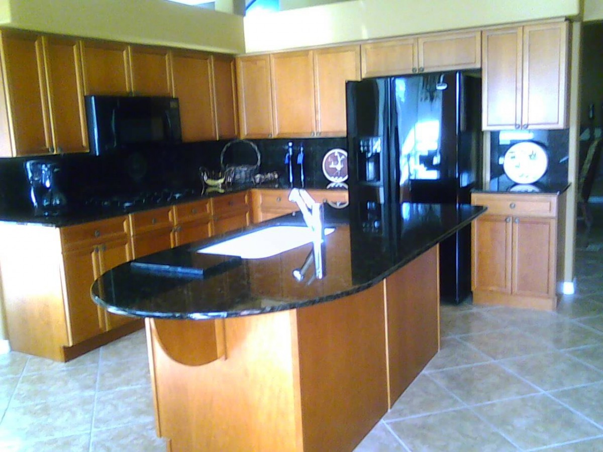A modern kitchen with wooden cabinets and a central island featuring black granite countertops.
