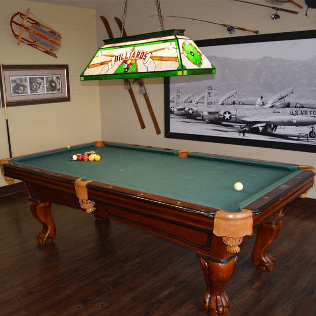 A vintage-styled game room featuring a classic pool table with green felt and wooden legs, under a retro light fixture.
