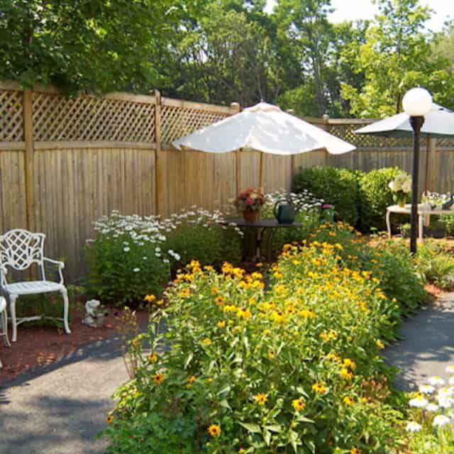 A serene garden with a variety of flowers, seating areas, and umbrellas for shade.