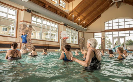 A group of seniors participating in a water aerobics class at an indoor pool, enjoying exercise and social interaction.