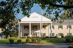 A colonial-style building with a grand entrance surrounded by trees and landscaped gardens.