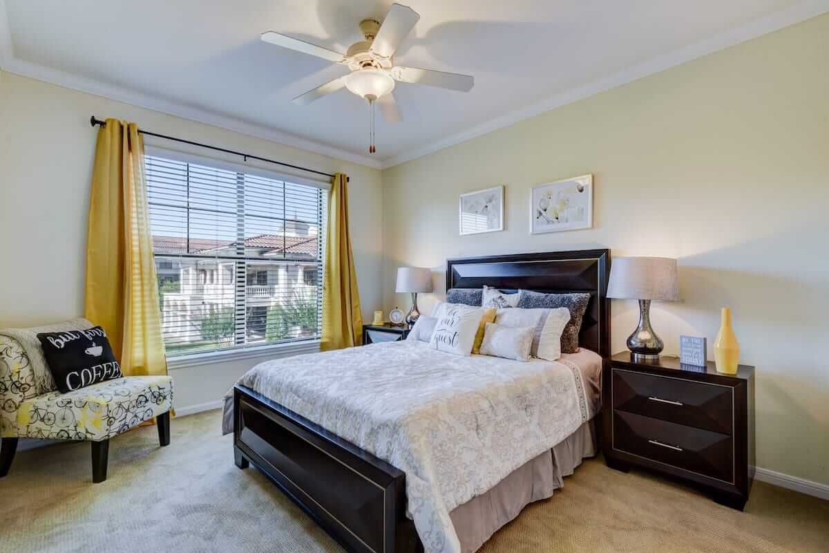 A cozy and well-lit bedroom featuring a large bed, bedside tables with lamps, and a ceiling fan.
