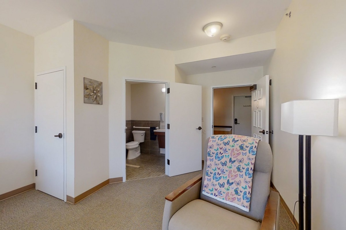 A cozy interior featuring a chair with a floral throw, multiple doorways, and a glimpse into a bathroom.