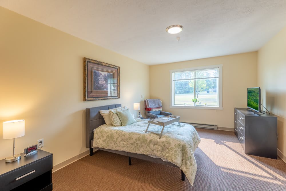 A cozy bedroom with a neatly made bed, a large window, and simple decor.