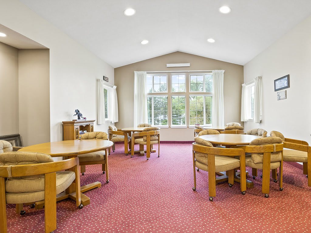 A bright room featuring multiple round tables and chairs, with large windows allowing natural light to fill the space.