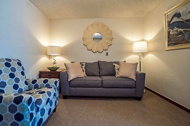 A cozy living room with a gray sofa, two lamps, and a decorative mirror on the wall.
