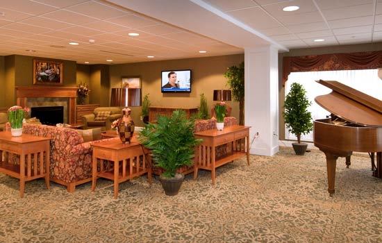 A cozy lobby with comfortable seating, wooden furniture, and green plants, featuring a television mounted on the wall.