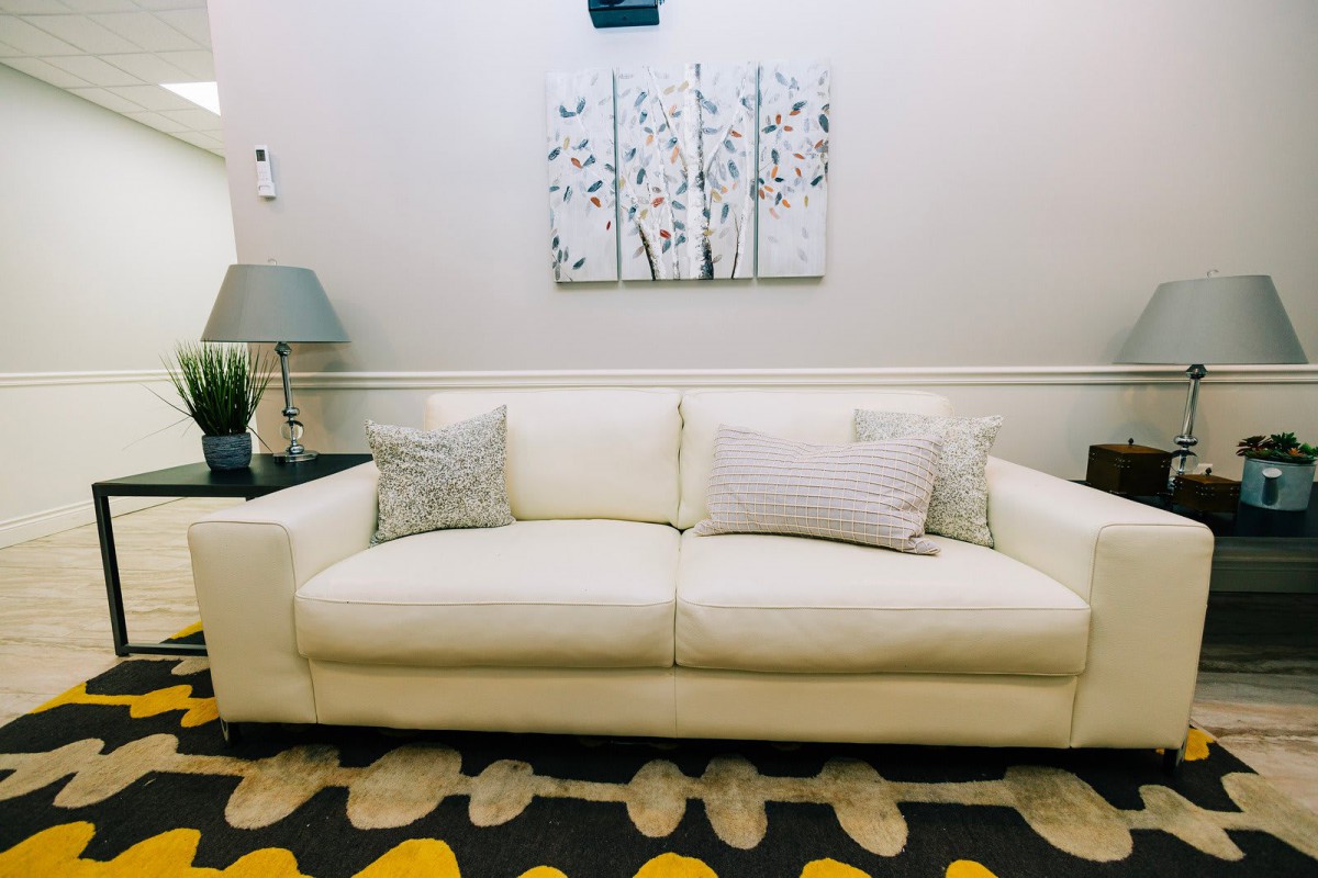A cozy living room featuring a white sofa with decorative pillows, modern artwork, and a patterned carpet.
