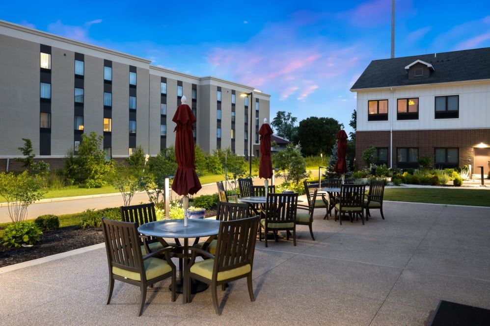An outdoor patio with tables and chairs, set against the backdrop of a building during evening time.