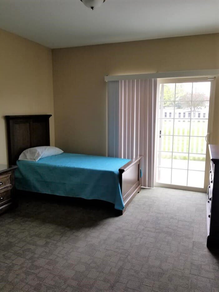 A simple bedroom with a single bed and a sliding glass door letting in natural light.
