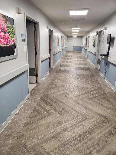 A well-lit interior hallway in a healthcare facility, featuring herringbone patterned flooring and decorative wall art.