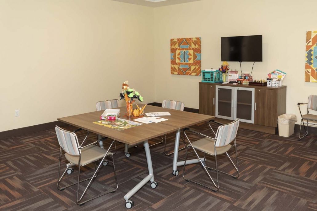 A modern meeting room with a central conference table, several chairs, and a television mounted on the wall.