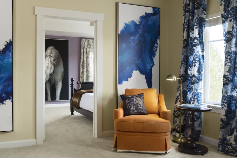 A modern living room featuring a vibrant blue abstract painting, cozy orange armchair, and stylish decor.