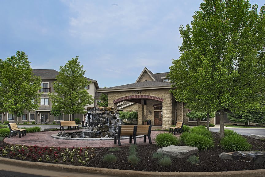 A peaceful outdoor area featuring a fountain, benches, and landscaped greenery in front of a building.