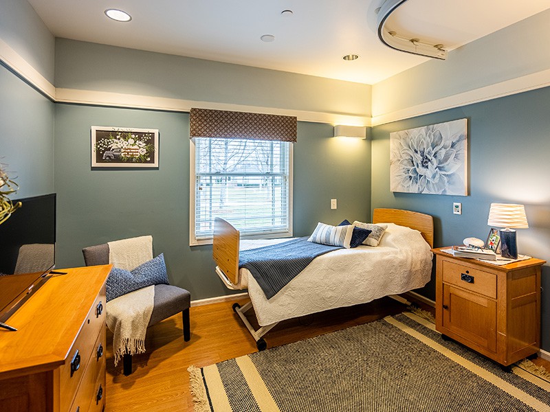 A modern and comfortable hospital room with a single bed, artwork on the walls, and a large window.