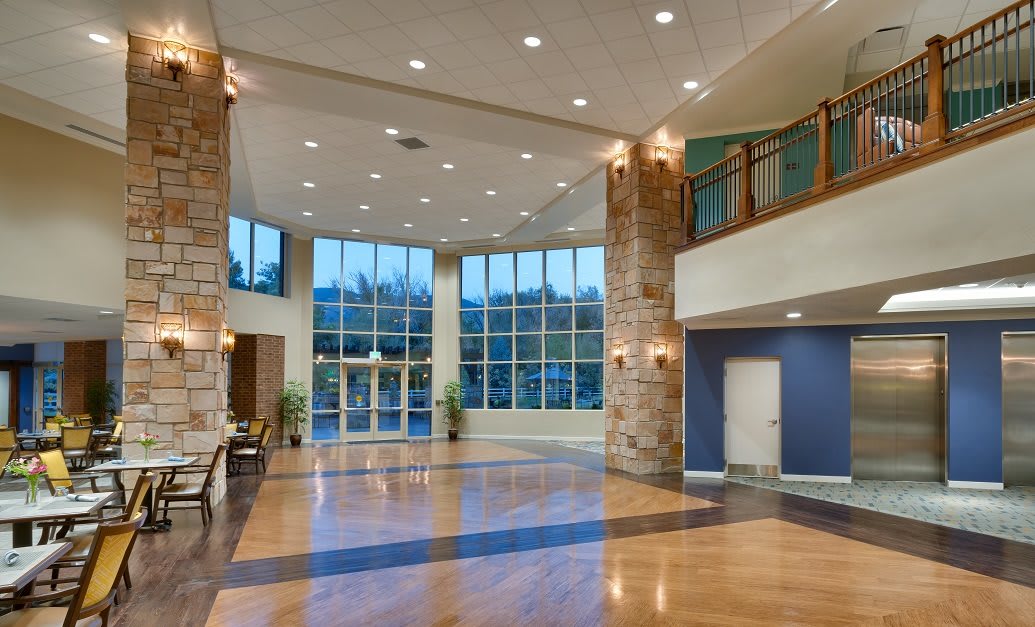 A modern and spacious lobby with wood flooring, stone columns, and ample lighting.