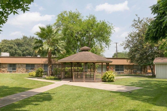 A serene outdoor space with a gazebo surrounded by lush greenery and trees.