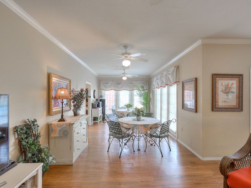 A bright and airy dining room with wooden flooring, featuring a round table set, large windows, and tasteful decor.