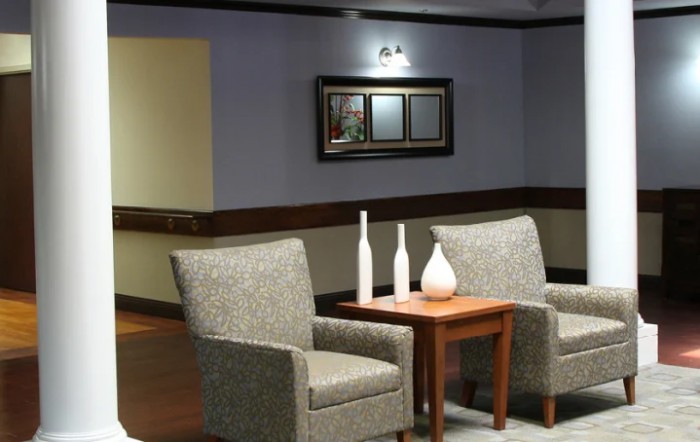 A cozy seating area with two chairs, a wooden table, decorative vases, and a wall mirror.