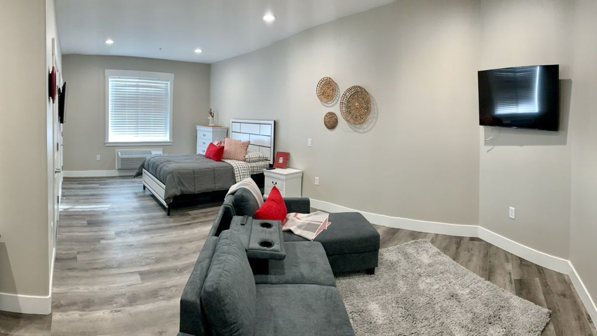 A modern bedroom with a cozy gray sofa, red accent pillows, and decorative wall pieces.