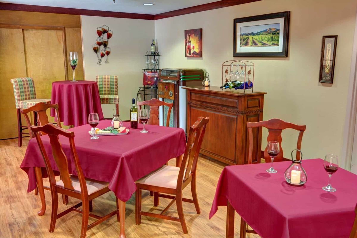 A cozy dining area with tables set for guests, featuring wine glasses and vibrant tablecloths.