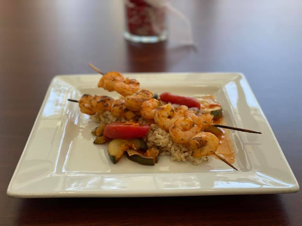 A dish of shrimp skewers with vegetables served on a bed of rice.