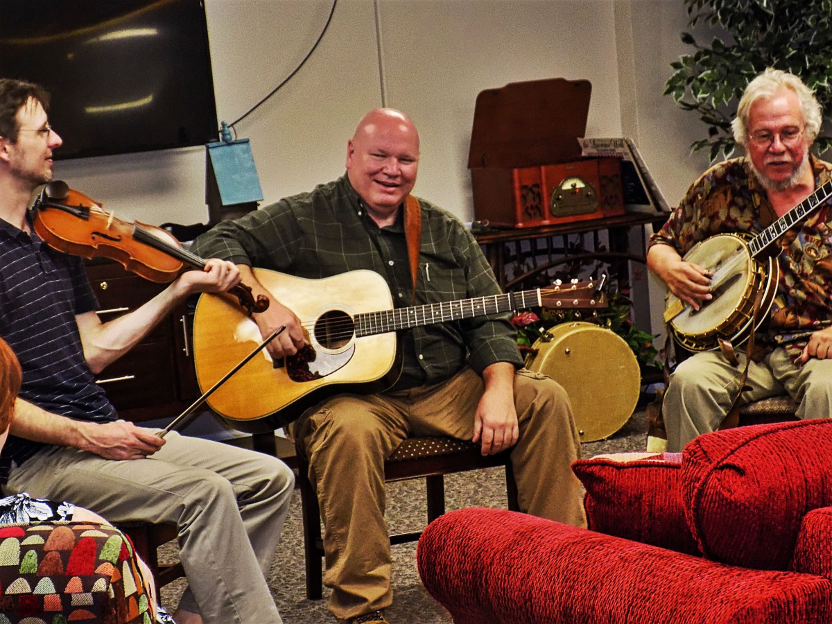 A group of musicians playing guitar, banjo, and violin in an intimate setting.