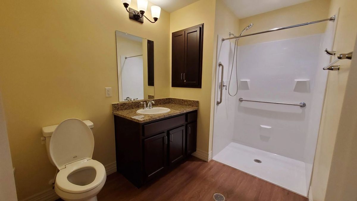 A modern bathroom with a dark wood vanity, sink, mirror, and a walk-in shower.