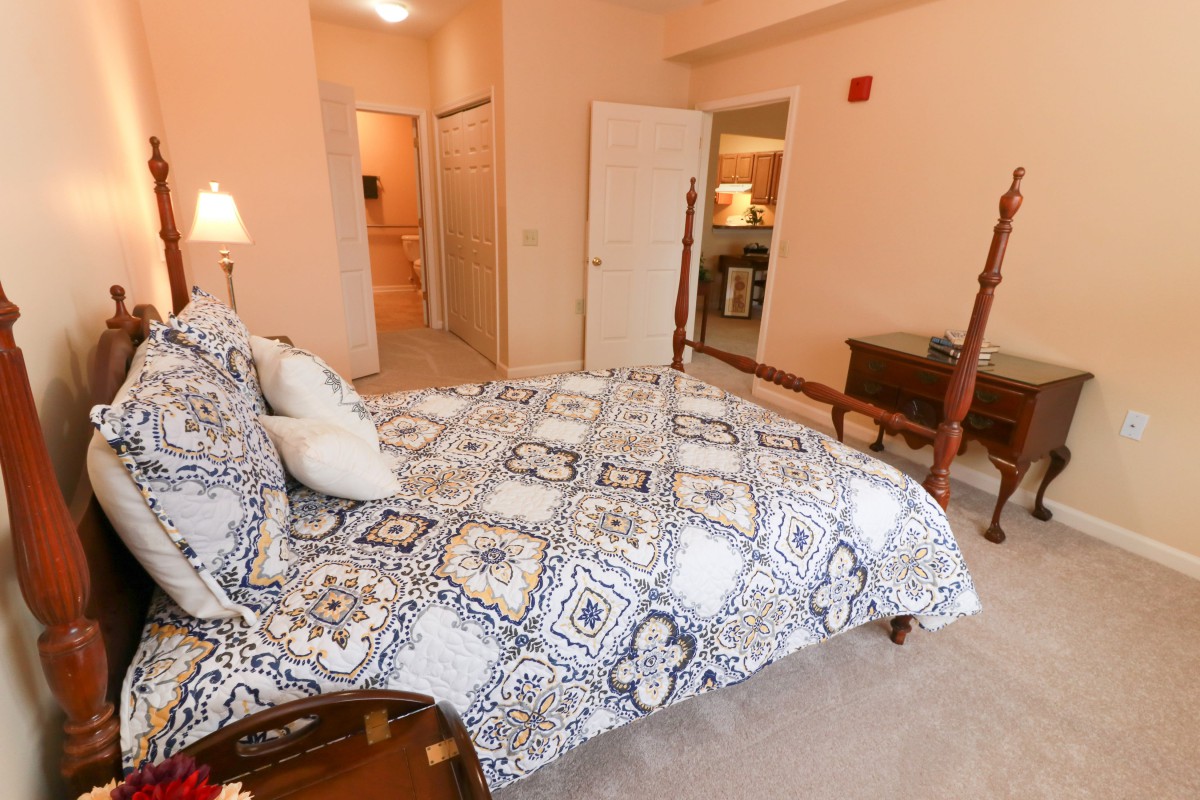 A cozy bedroom featuring a four-poster bed with patterned bedding and a carpeted floor.