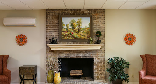 A cozy living room setup featuring a brick fireplace, adorned with a beautiful landscape painting and decorative vases.