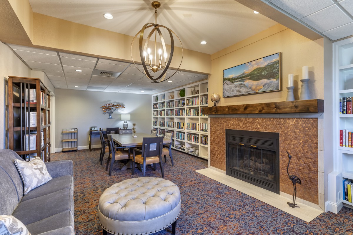 A cozy living room features a warm fireplace, bookshelves filled with books, and a dining table illuminated by an elegant chandelier.
