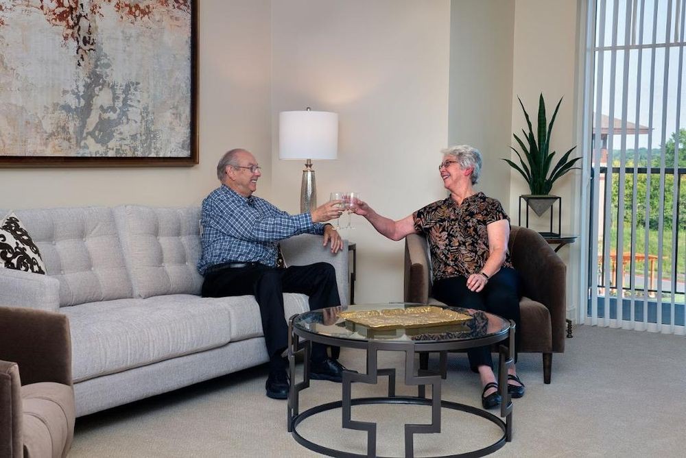 An elderly couple sitting in a cozy living room, smiling and holding hands, surrounded by modern decor.