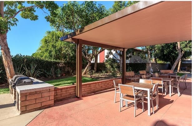 A serene backyard patio with a canopy and outdoor furniture, surrounded by lush greenery.